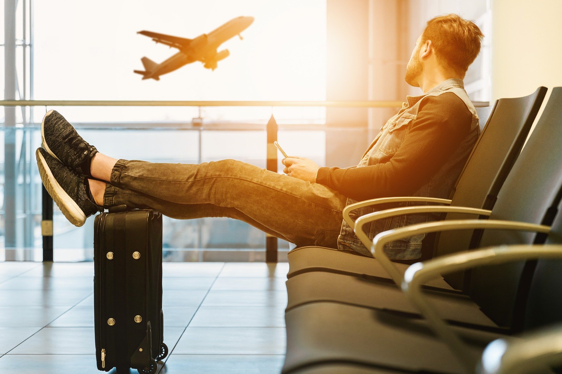 seorang pria duduk dengan kaki tertahan koper melihat pesawat